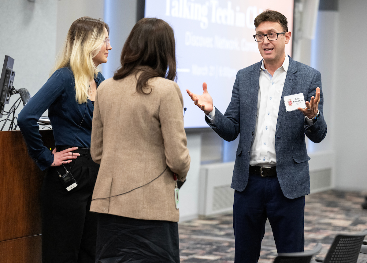 Image of speaker Ross Freedman interacting with two individuals at an event